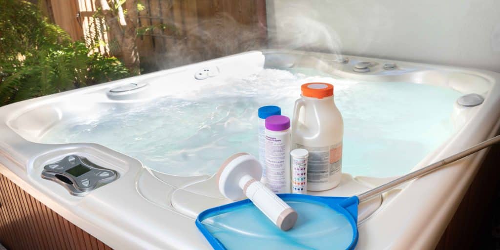 Professional spa cleaning chemicals, test strips, and skimmer net on hot tub edge by PureWave Pools in Santa Cruz